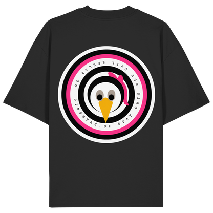 Die Rückansicht eines schwarzen Oversized-T-Shirts mit einem großen, kreisrunden Grafik-Print im Zentrum. Das Motiv zeigt das kreisrunde Pingstas-Logo in den Farben Schwarz, Weiß und Pink, in dessen Mitte der Pinguin-Charakter mit einer pinken Schleife abgebildet ist. Auf den äußeren Ringen des Logos ist der Schriftzug „PINGSTAS.DE – STAY CUTE GET EVIL – BERLIN 26“ zu lesen. Das Produktbild ist vor einem transparenten, karierten Hintergrund freigestellt